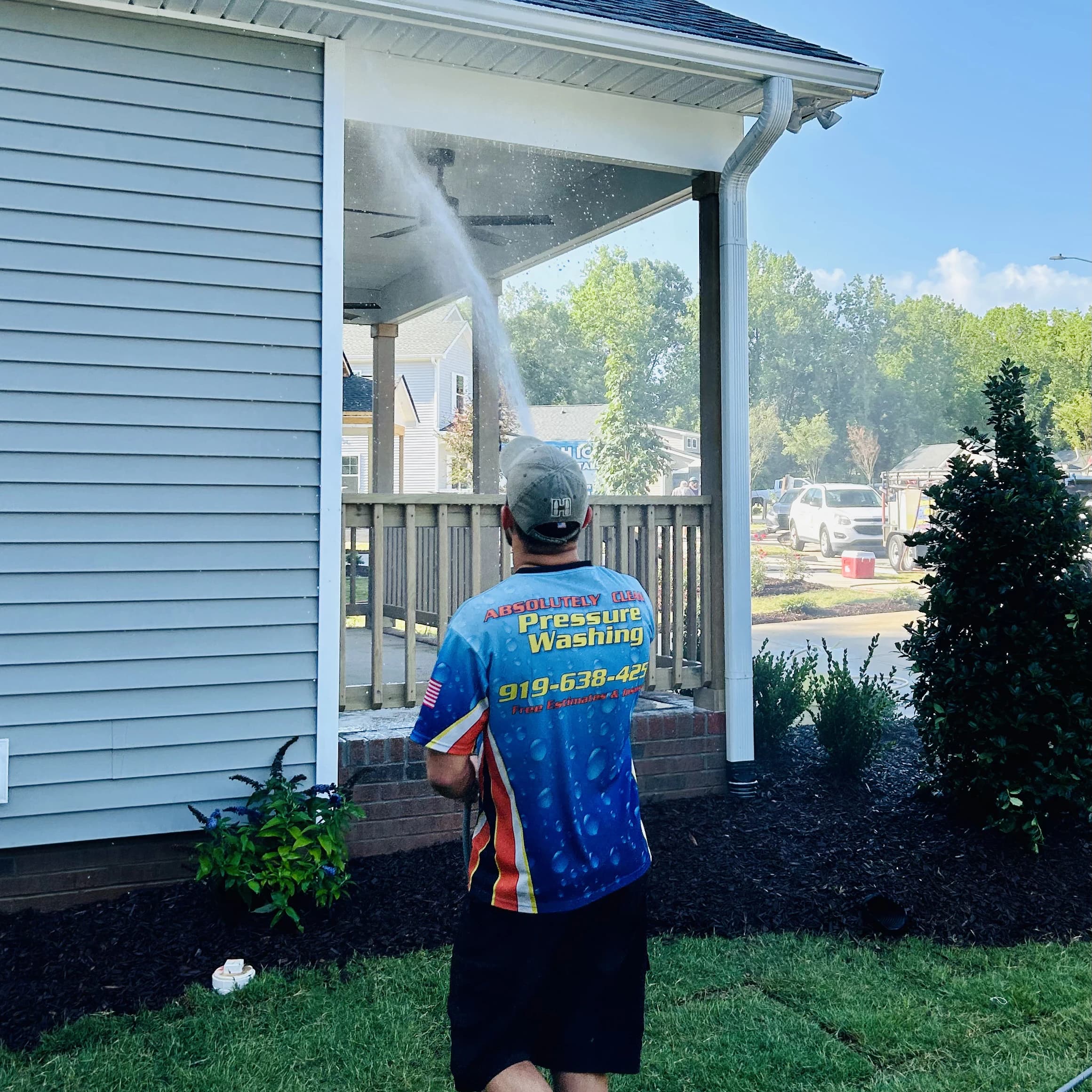 Technician rinsing house siding and a covered porch